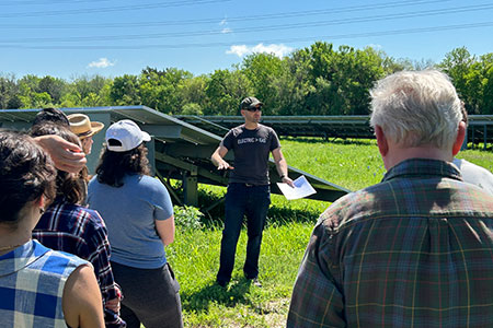 Man speaking to group in front of solar panels