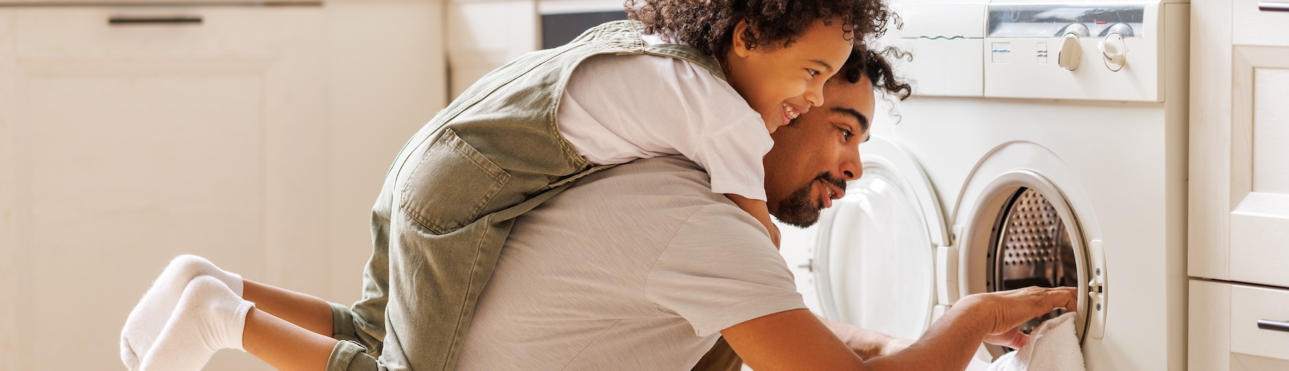 Man getting clothes out of dryer while child is on his back.